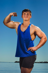 the athlete on the beach posing on blue sky background. Strong hands