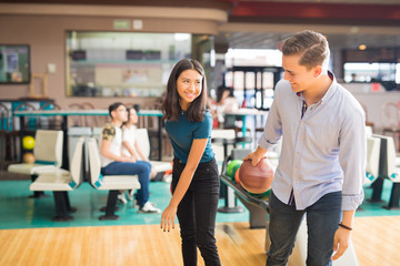 Smiling Boy Teaching Friend To Play Bowling In Club