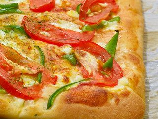 Pizza with tomato and green pepper. Fresh baked piece of pizza with red tomatoes, green pepper and cheeze on the parchment paper.