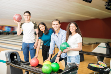 Friends Picking Up Balls While Having Fun At Bowling Alley
