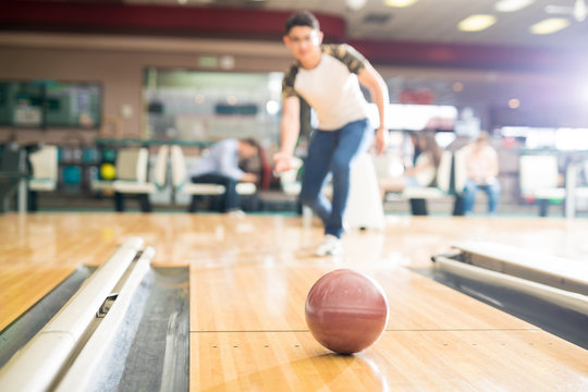 Teenage boy Bowling In Club With Focus On Brown Ball