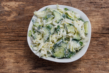 Spring salad with cabbage, cucumber, green onion, parsley and mayonnaise on wooden table