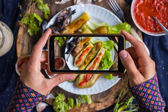 Hands take smartphone food photo of roasted grilled eggplants. Lunch or dinner. Phone photography of food for social media or blogging. Raw vegan vegetarian healthy food.