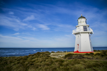 Travel New Zealand. Scenic view of white lighthouse on coast, ocean, outdoor background. Popular tourist attraction, Waipapa Point Lighthouse located at Southland, South Island. Travel concept.