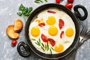 Fried eggs with tomatoes in a frying pan, gray background.Flat lay