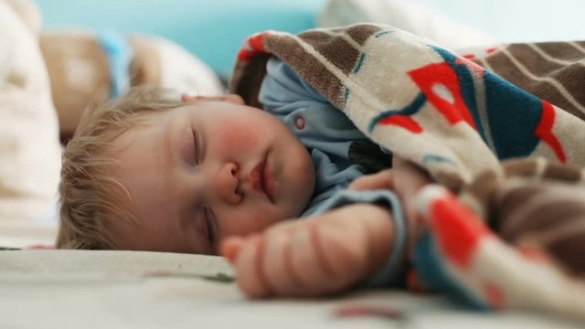 adorable blonde caucasian baby boy sleeping calm at home cute child covered with blanket having rest chubby cheeks closed eyes sweet face day light inside relaxation dream children healthcare serene