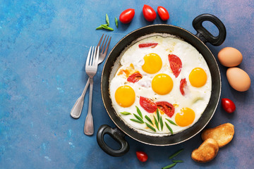 Breakfast fried eggs with tomatoes, served in a pan on a blue background. Top view, space for text.