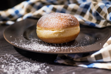 Fresh home donute on a brown plate sprinkled and checkered towel with powdered sugar.