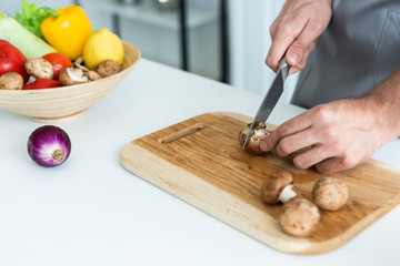 close-up partial view of man cutting fresh mushrooms on wooden cutting board