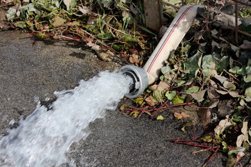 Fire department water hose used for pumping flood water from garden through wire fence on sidewalk