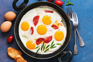 Fried eggs with tomatoes served in a pan with toast on a blue background. Flat lay, tinted photo.