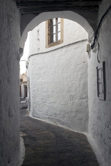 A view of a street with an arch and white stone buildings with windows in the island of Patmos, Greece