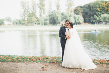 Stylish couple of happy newlyweds walking in the park on their wedding day with bouquet