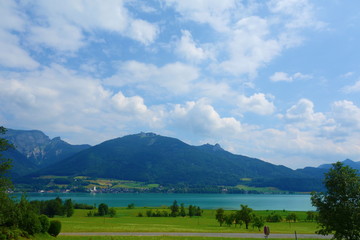 Lake called Wolfgangsee in Austria with mountains in the background and clouds on the sky and grass in the front