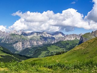 Fototapeta premium Picturesque July Alpine view from the Sella Pass in the Dolomites with big cumulus clouds, in South Tyrol, Italy