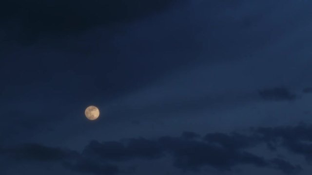 Time lapse of moving dark blue clouds and shining moon. Dramatic cloudy sky. Cloudscape at nighttime