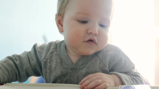 Happy toddler standing himself near the sofa over white bright sun light background playful baby boy sweet chubby cheeks blue eyes looking at camera parenting kid caucasian infant portrait closeup
