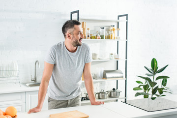 side view of smiling man standing near table on kitchen