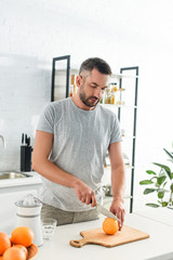 focused adult man cutting orange by knife on kitchen