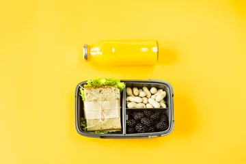  Lunchbox met voedsel - sandwich, noten en bessen - naast een fles sinaasappelsap op een gele achtergrond. Bovenaanzicht, plat gelegd, © svitlini
