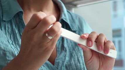 Woman filing nail with nail file while home manicure. Home manicure and nail care. Woman doing yourself manicure close up.