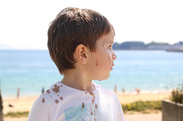 niño de perfil manchado de helado de chocolate que le tiraron por encima en la playa