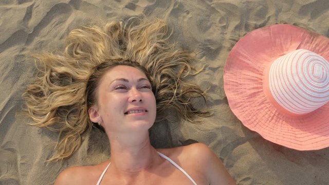 The woman lies directly on the sandy beach. He looks at the camera, smiles, laughs. The girl yawns funny. View from above.