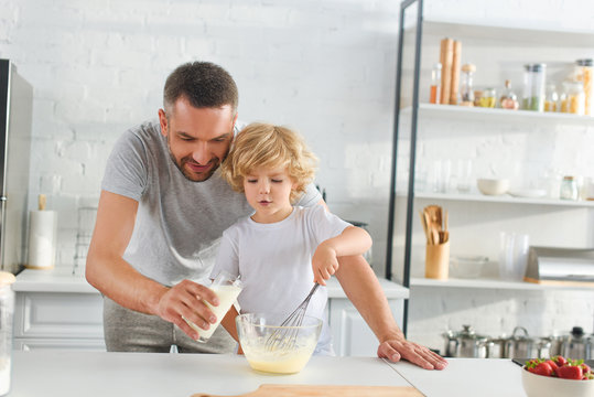 little boy whisking dough while his father pouring milk into bowl at kitchen