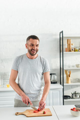 smiling adult man cutting strawberry by knife on table at kitchen
