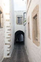 Fototapeta premium A view of a noarrow street with arch and windows and doors with white wall stone architecture of the island Patmos, Greece