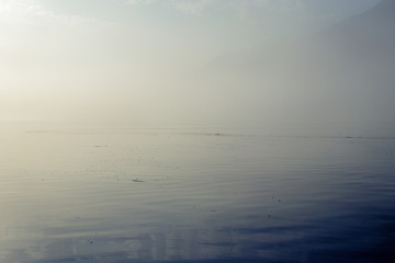 Early morning sunrise on lake Como in Italy. The sun is breaking through as the fog starts to disappear from the surface of the water. After that it is time to wait for the wind to go windsurfing