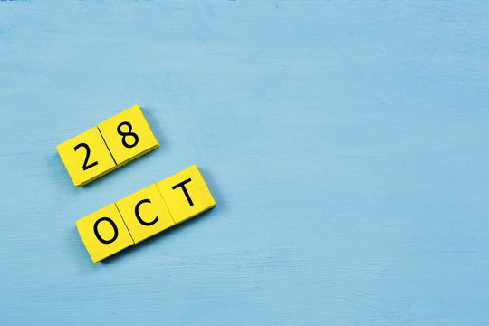OCT 28, yellow cube calendar on blue wooden surface with copy space