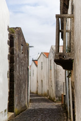 View into a paved arched alley with white and dark country houses, in the foreground a small balcony - Location: Azores, Corvo Island