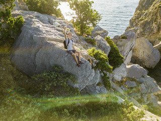 young teenager boy sitting on the mountain edge with backpack making a self portrait