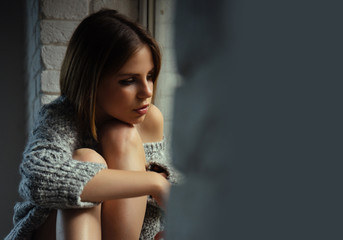 Obraz premium Woman with makeup on pretty face look throught window. Woman sit with legs on window sill. pretty woman, copy space