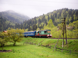 In the mountains a green locomotive with blue wagons. The train goes to the Carpathians