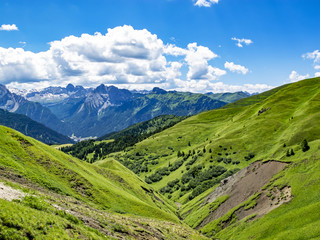 Idyllic July green Alpine view from the Sella Pass in the Dolomites with big cumulus clouds, South Tyrol, Italy
