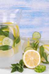 Refreshing water with lemon and cucumber in a glass jug next to fresh lemon on a blue wooden background