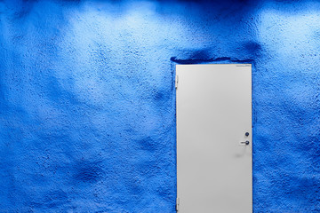 White door with blue wall with shadows and light. Copy space.