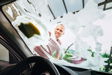 Man washes car front windows with soap foam