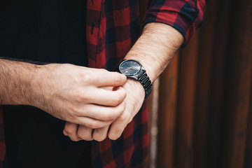 close up fashion details, young fashionable man wearing a red checked shirt and a black analog wrist watch. street style detail of an elegant clock.