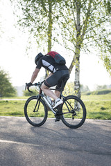 Obraz premium Back of a cyclist with a backpack while riding in the city on a bike. Man in sportswear and a helmet rides the city park.