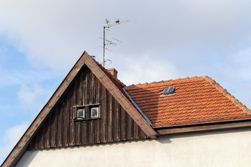Pigeons on antenna on old red ceramic roof under cloudy sky at sunset