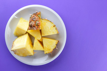 Pieces of pineapple on a white plate, chopped fresh pineapple on a violet background, salad of tropical fruits for breakfast, vegetarian food, copy space