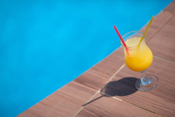 glass of yellow juice with ice against the background of the pool in summer