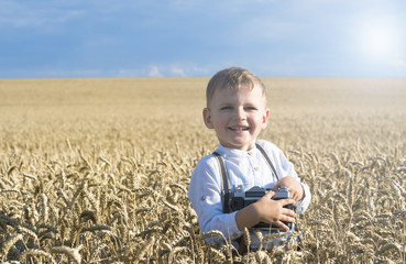 .Cute boy in rye field taking photos with retro camera.