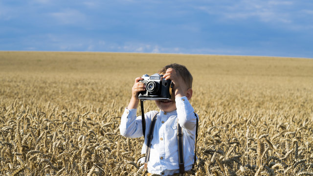 Cute boy in rye field taking photos with retro camera.