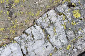 Close up directly above view of mountain rock, grеy mineral with crystal structure, cracks and spots of yellow Alpine lichen