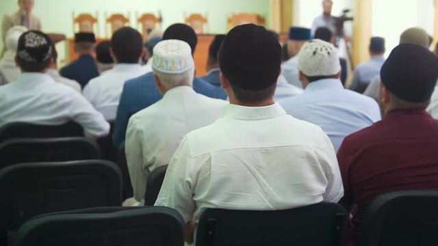 Rear view of muslim men in skullcaps sitting at the mass rally