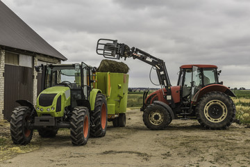 Agricultural machinery and equipment.The tractor with the loader loads a bale of silage in the distributor of mixed fodders for cows.Podlasie, Poland.